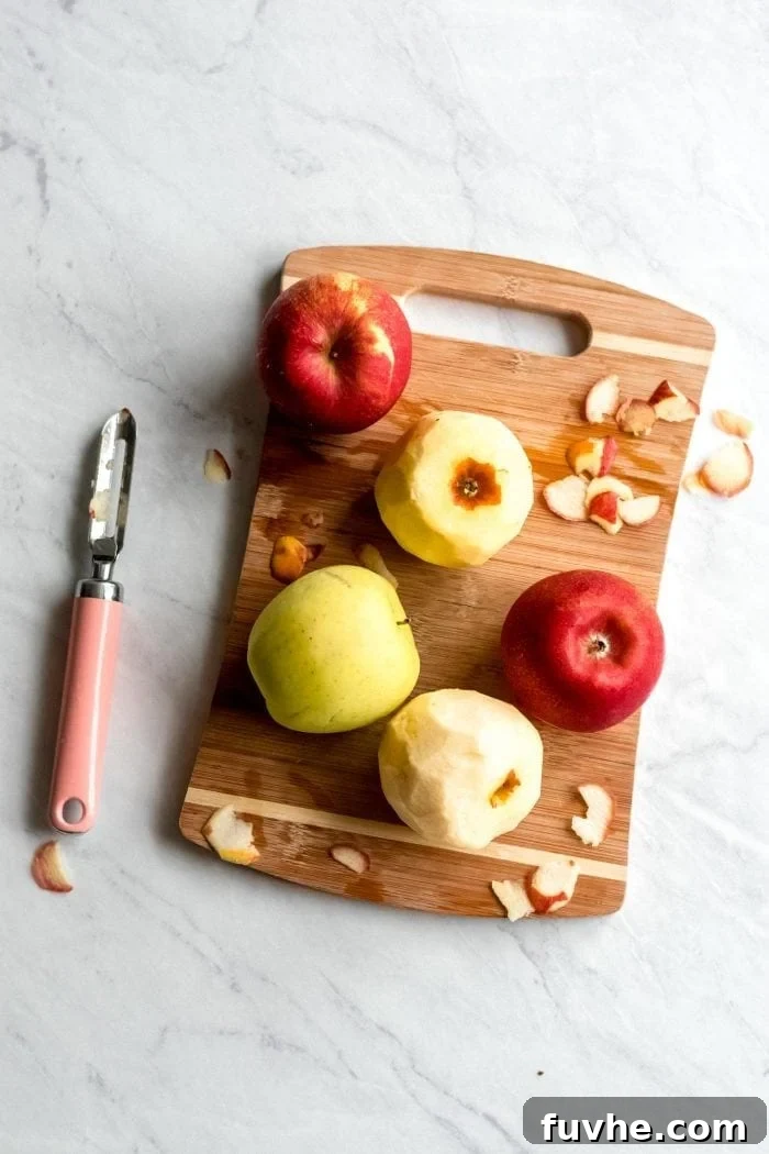 5 apples on a cutting board with an apple peeler.
