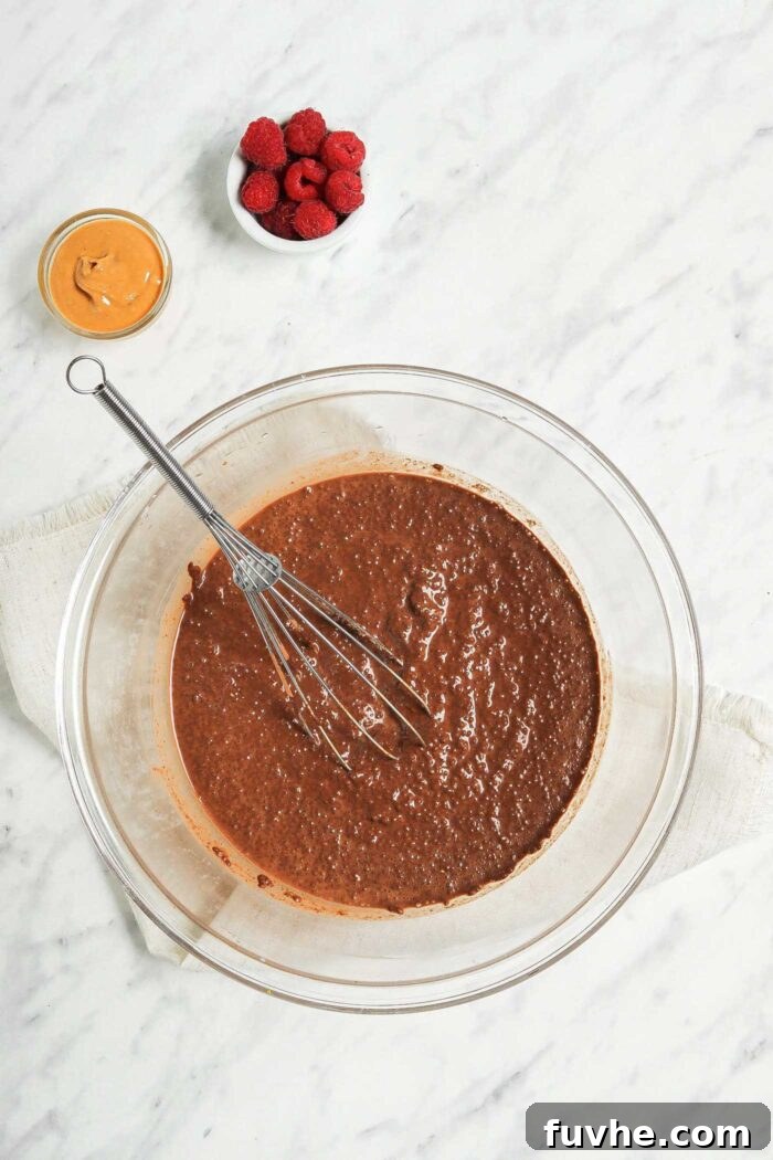 A large glass mixing bowl filled with chocolate chia pudding mixture, with a whisk resting inside, ready for chilling.