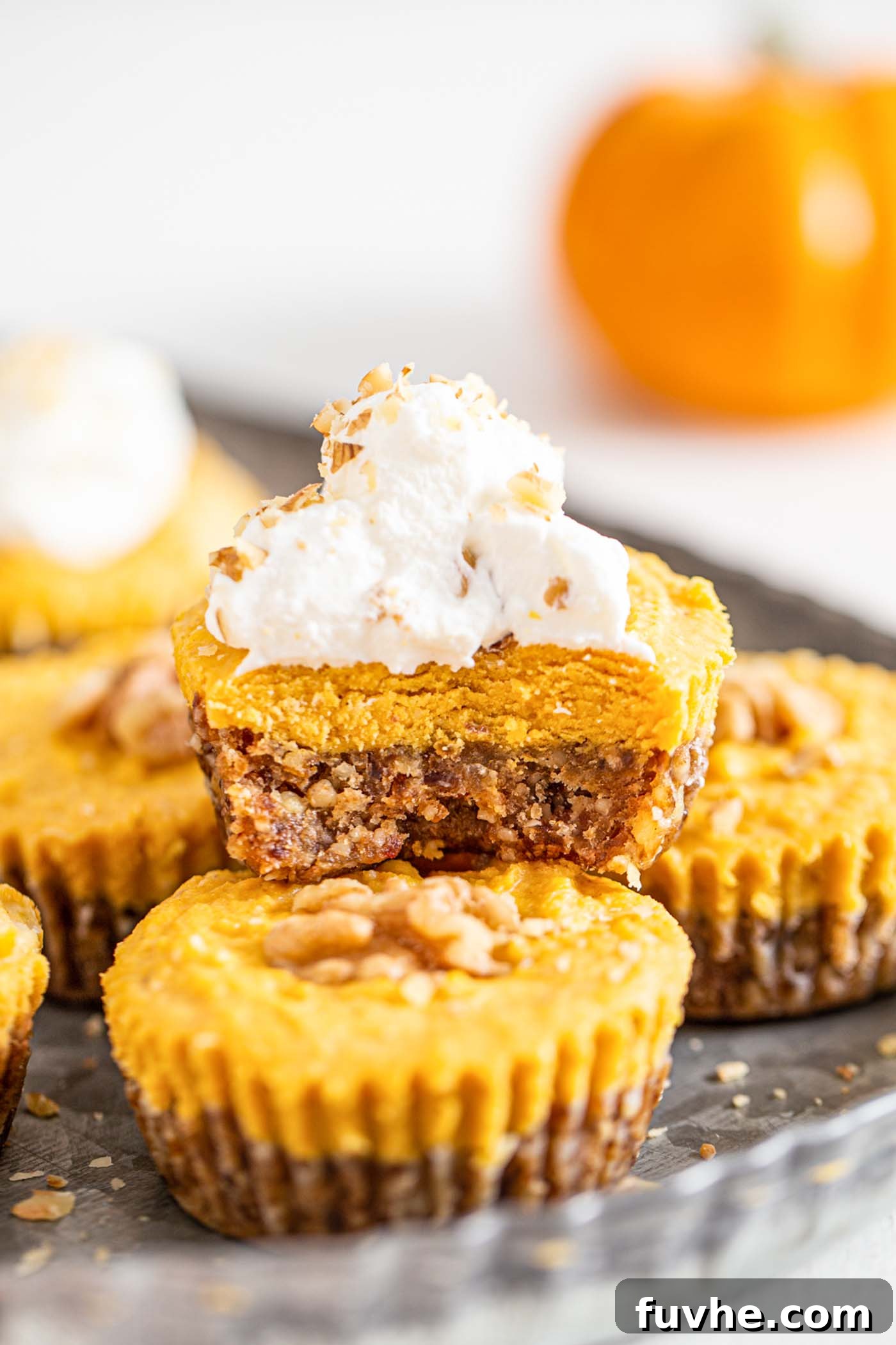 A perfectly portioned vegan no-bake pumpkin pie tart, with a small bite taken to reveal its creamy interior. A generous dollop of dairy-free whipped cream adorns the top.