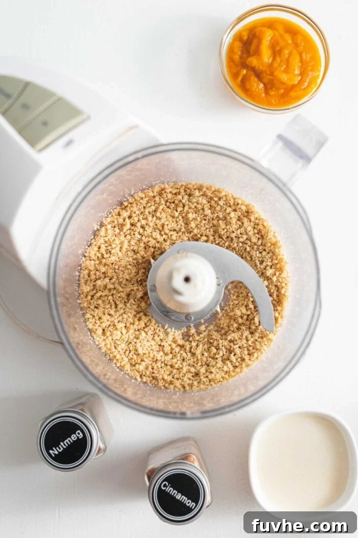 Finely blended walnuts processed into crumbs within a food processor container, with a can of pumpkin puree and a bowl of coconut milk visible nearby.