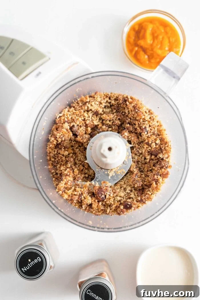 A close-up view of walnuts and dates thoroughly blended together inside a food processor container, forming a sticky, crumbly mixture.