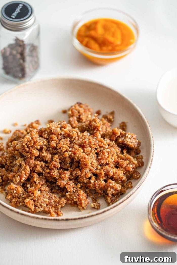 A bowl containing crumbly yet sticky dough made from walnuts and dates, infused with spices. Small bowls of maple syrup and pumpkin puree are placed alongside, ready for the next step.