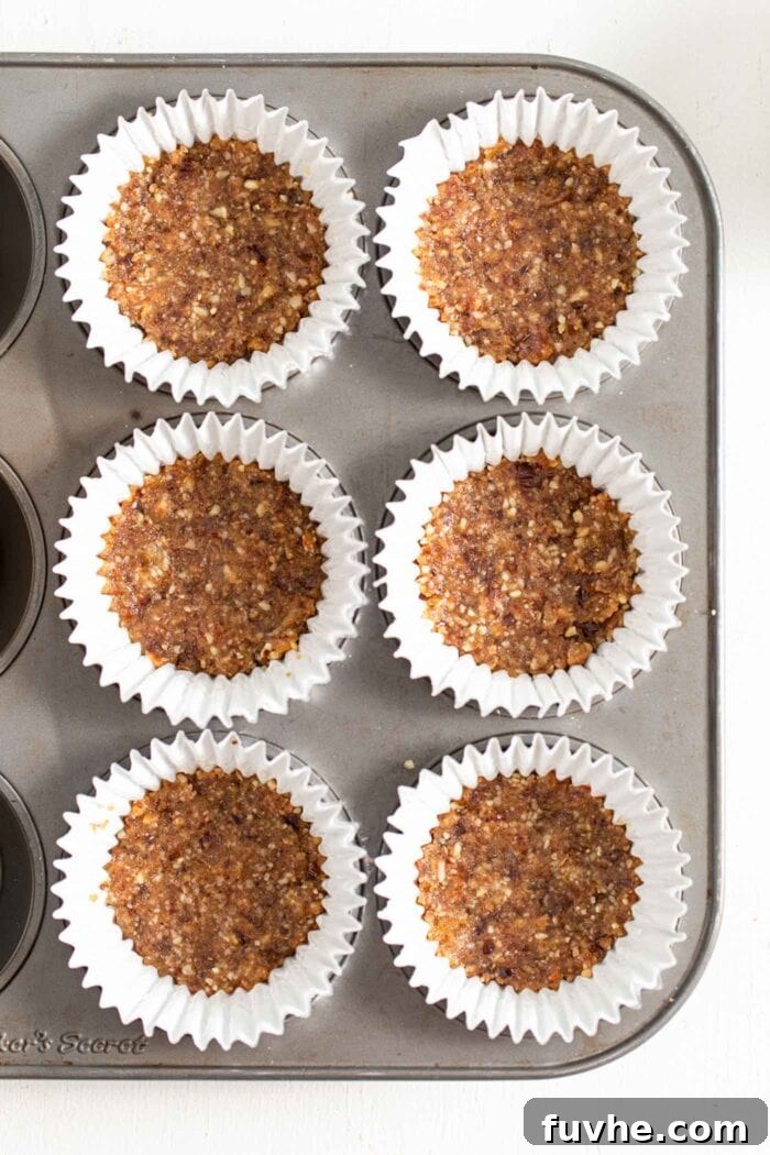An overhead shot showcasing six cupcake liners arranged in a muffin tin, each containing a perfectly pressed layer of walnut and date dough, ready for the filling.