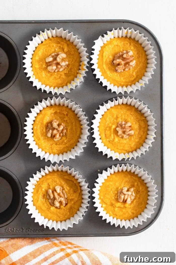 An overhead view of six perfectly formed pumpkin tarts, each topped with a delicate scattering of walnuts, nestled in cupcake liners within a muffin tin.