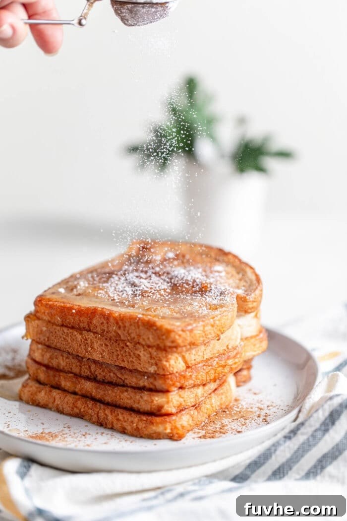 Tropical Coconut Vegan French Toast 7 A beautifully stacked pile of vegan French toast being dusted with powdered sugar, ready to be served.