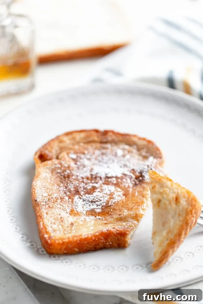 Tropical Coconut Vegan French Toast 8 A single slice of vegan French toast, beautifully golden, drizzled with maple syrup and sprinkled with sugar, on a white plate.