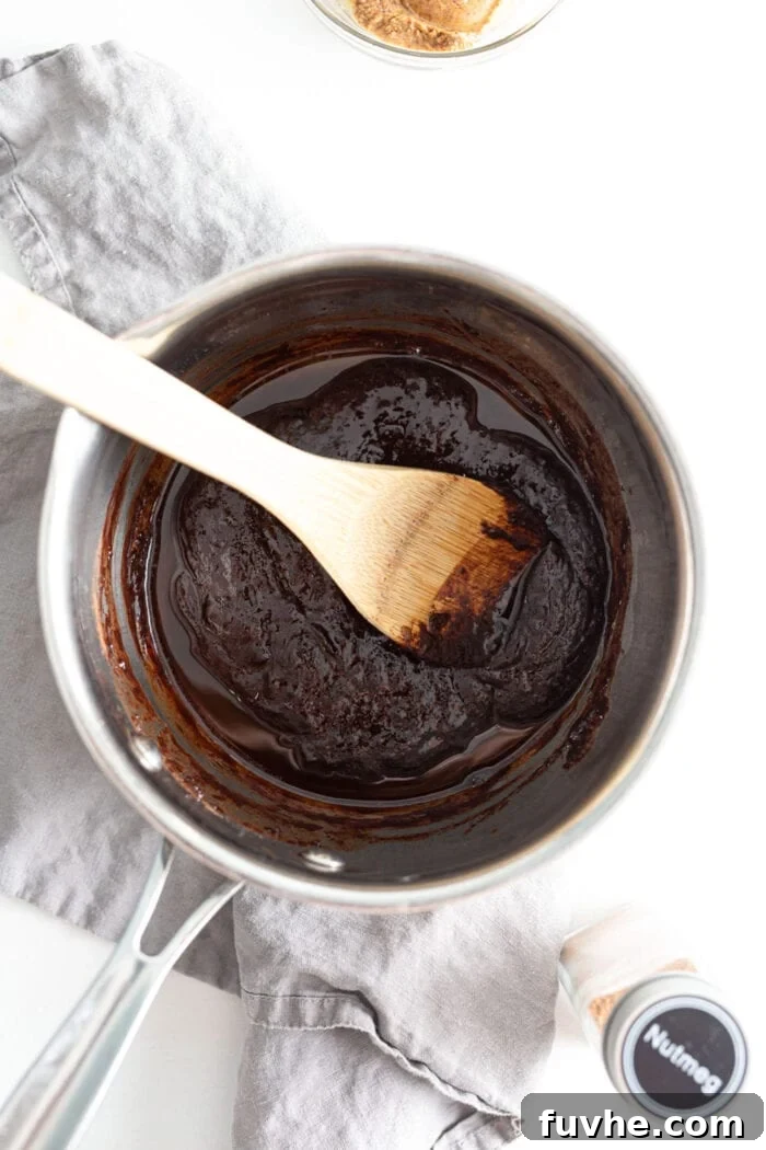 A saucepan on the stove containing a melted chocolate mixture, with a wooden spoon resting inside, ready for the next step.