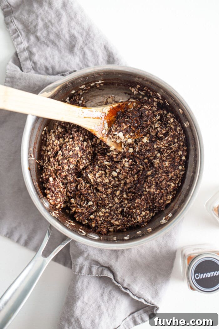 A saucepan filled with a rich chocolate and oat mixture, with a spoon resting in the pan, showing the ready-to-form cookie dough.