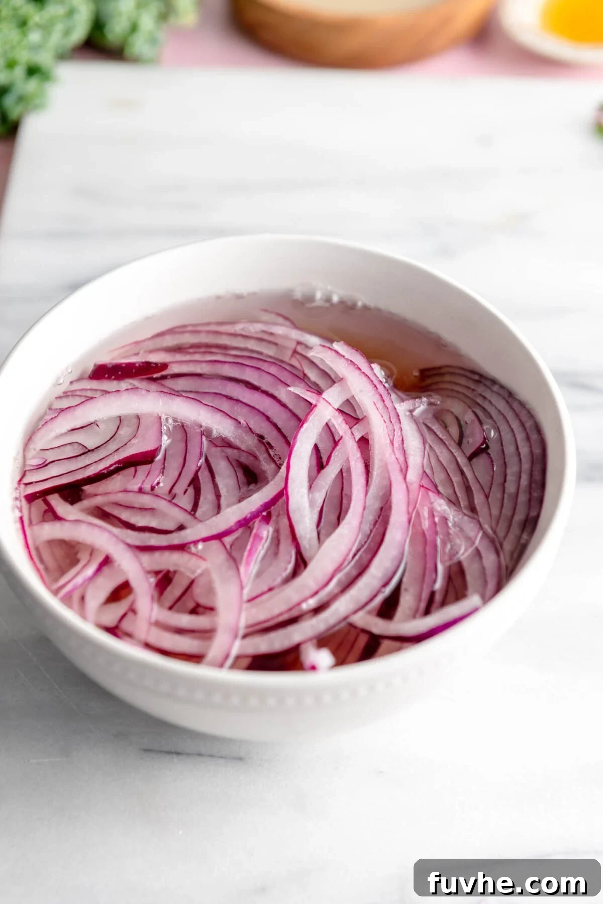 Thinly sliced red onion soaking in a bowl of water, preparing to be pickled for a flavorful addition to the wild rice bowl.