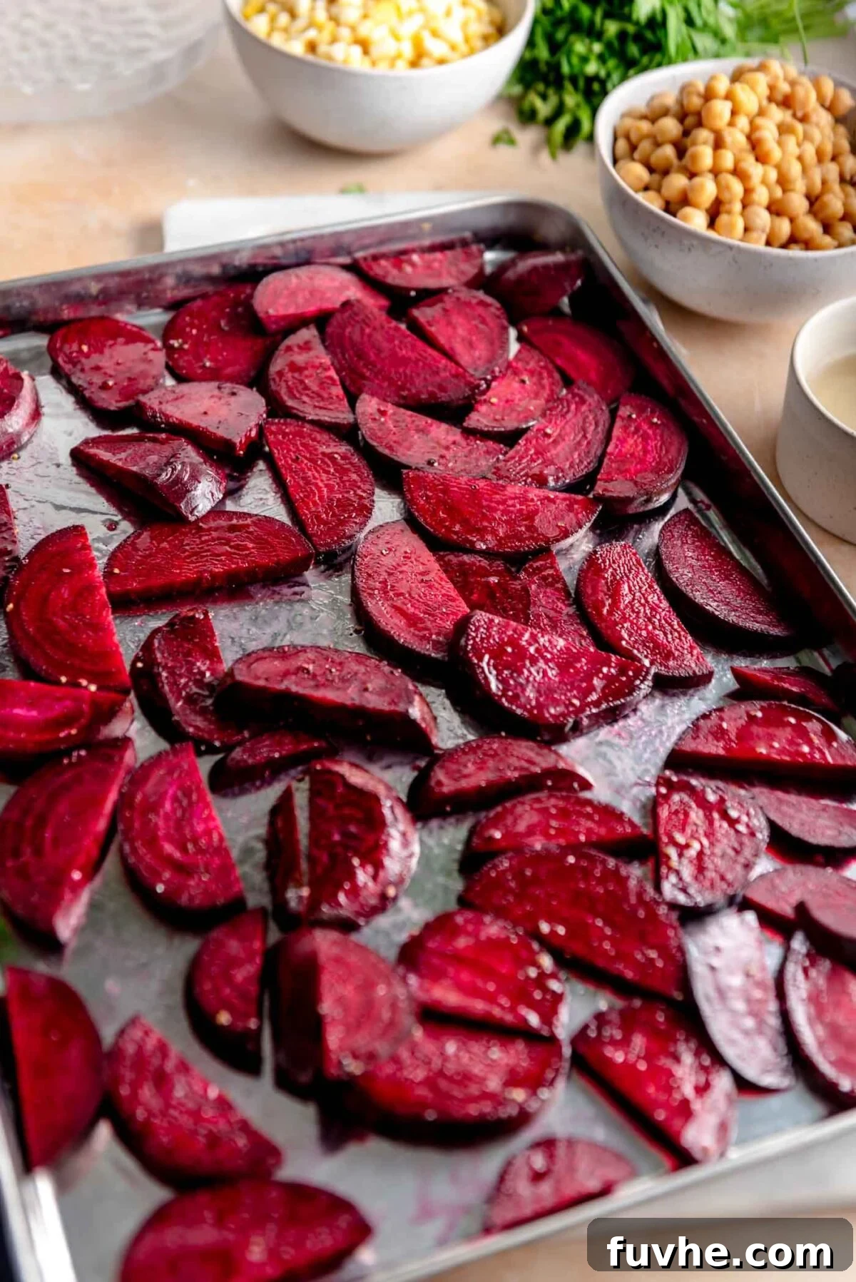 Thinly sliced beets tossed with oil, salt, and pepper, arranged in a single layer on a large baking sheet, ready for roasting.