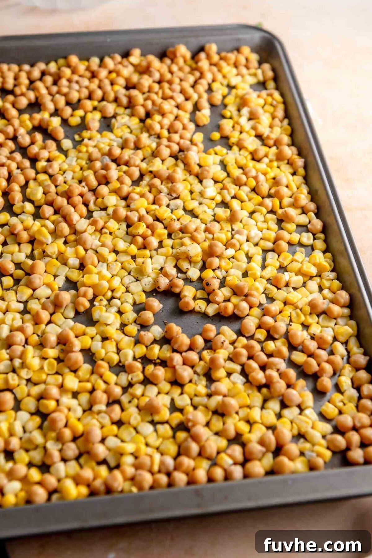 Chickpeas and corn seasoned with olive oil, salt, and pepper, spread on a baking sheet, ready to be roasted alongside the beets.