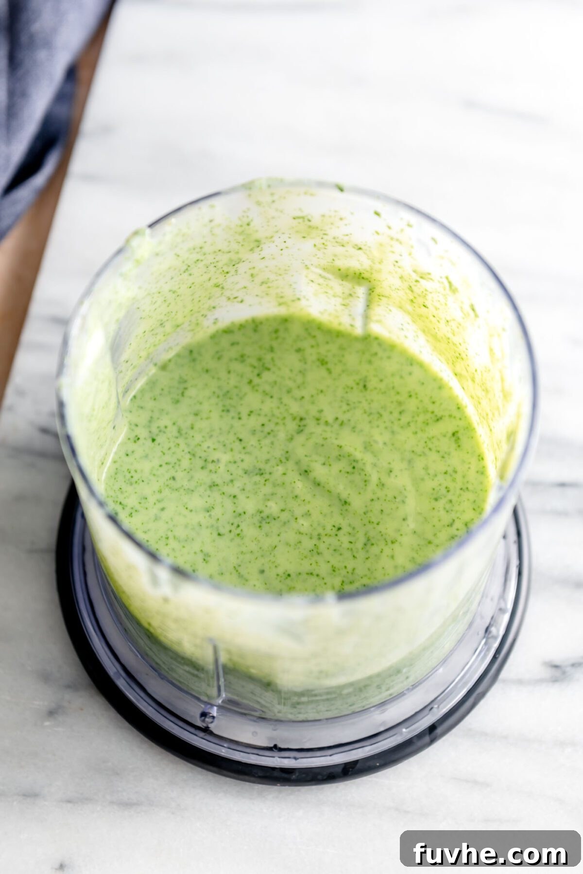 All the vibrant ingredients for the herb lemon yogurt dressing, including fresh parsley, cilantro, lemon, garlic, and plant-based yogurt, in a mini food processor, ready to be blended until smooth.