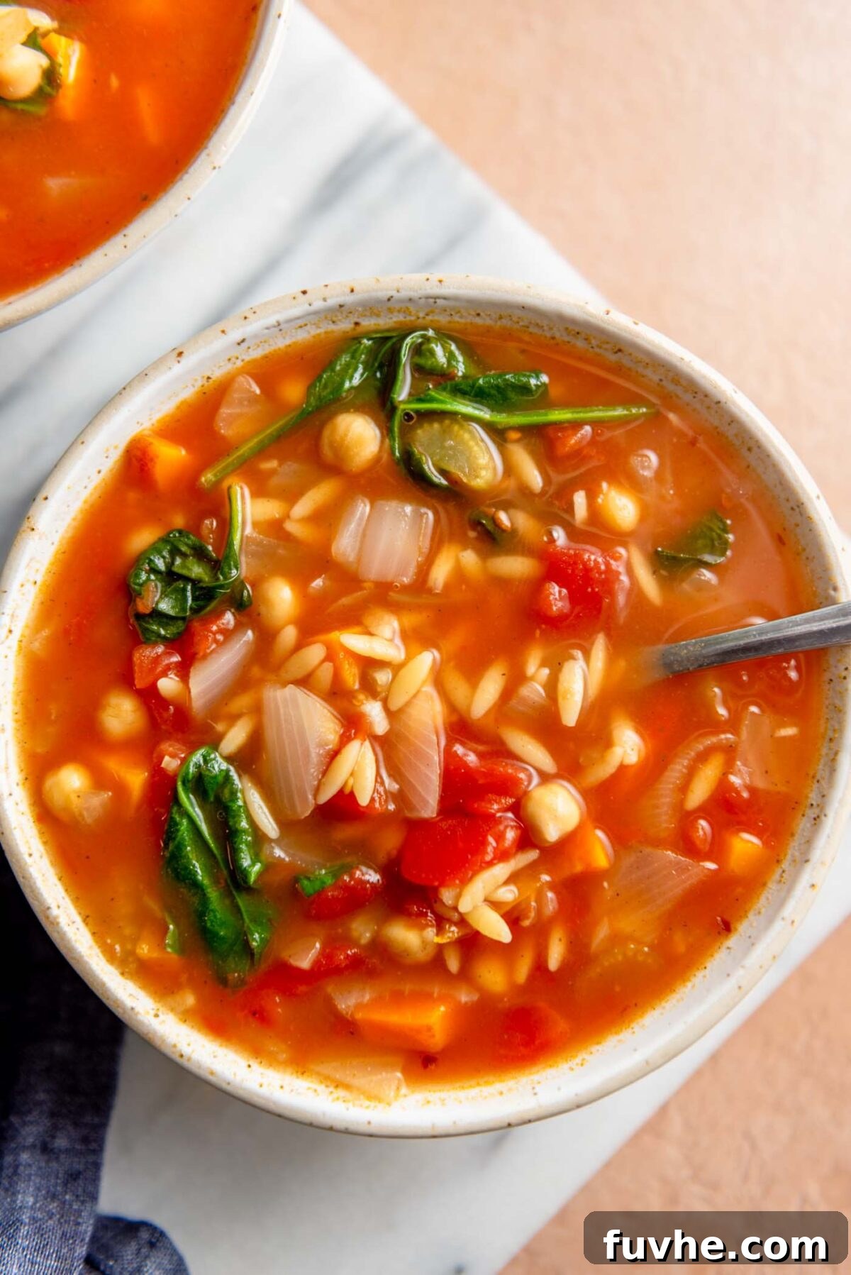 Vibrant Tomato Orzo Soup 2 A vibrant bowl of tomato orzo spinach soup, garnished with fresh herbs, resting on a rustic marble cutting board.