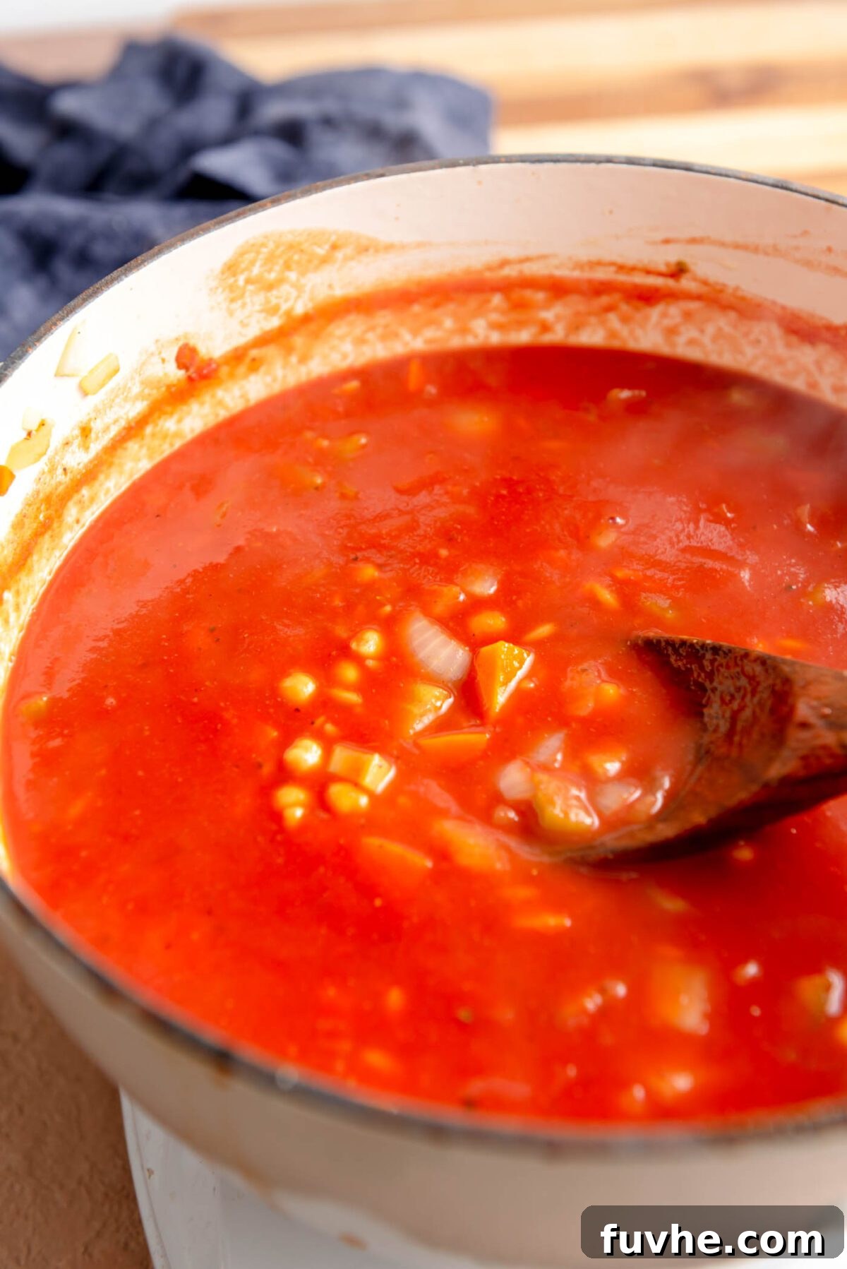 Vibrant Tomato Orzo Soup 7 Orzo pasta and chickpeas happily cooking in a vibrant tomato broth within a large soup pot, stirred with a wooden spoon.