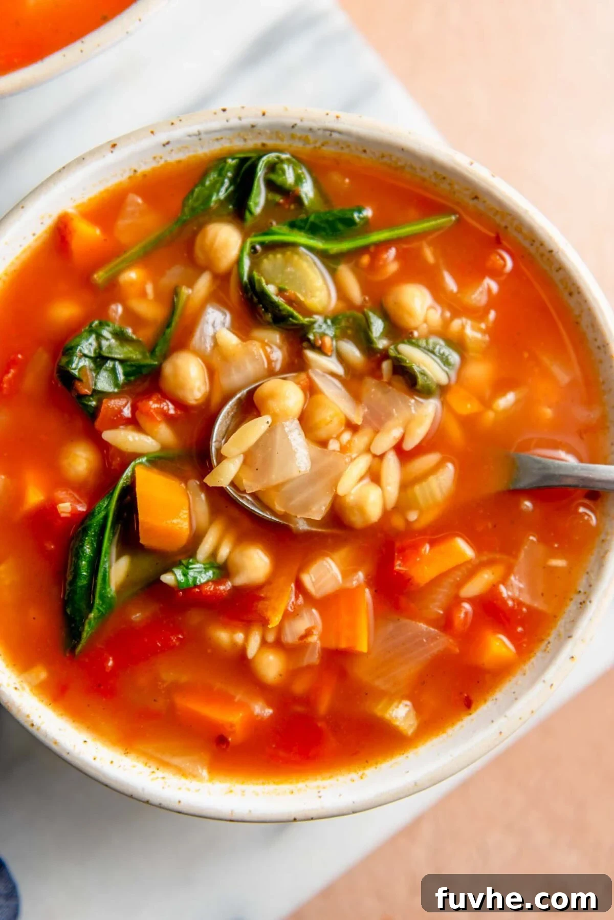 Vibrant Tomato Orzo Soup 9 A steaming bowl of comforting tomato orzo soup, rich with spinach and chickpeas, served on a wooden cutting board with a spoon ready to enjoy.