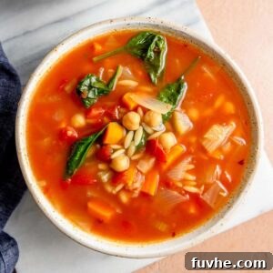 A comforting bowl of tomato orzo spinach soup, ready to be enjoyed, artfully placed on a marble cutting board.