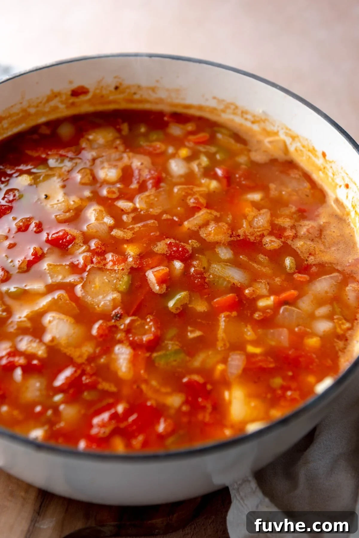 Ultimate Vegan Enchilada Soup 6 A large pot filled with a rich, tomato-based soup, featuring sautéed onions, bell peppers, pinto beans, corn, and sweet potato, simmering on the stove.