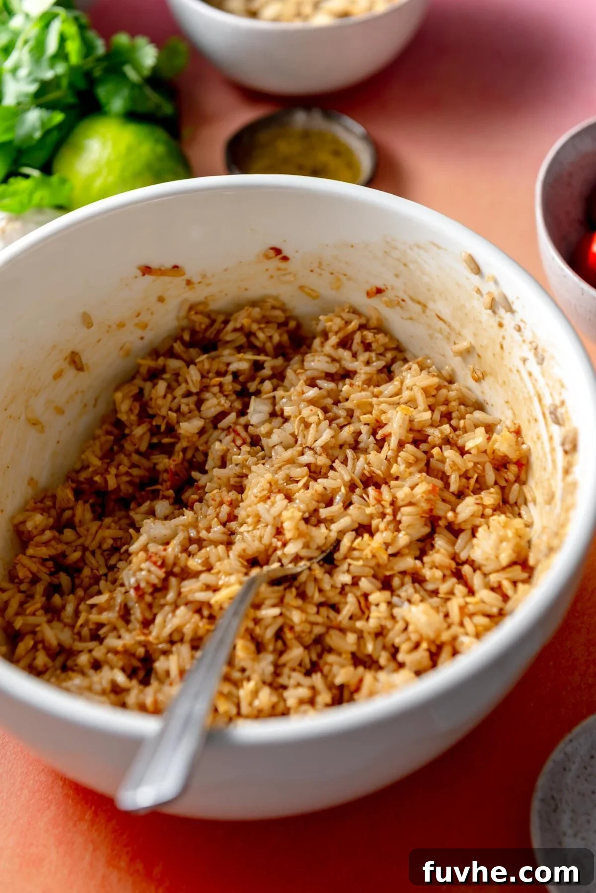 Cooked rice in a bowl, thoroughly mixed with red curry paste and coconut flakes, ready to be spread and baked.