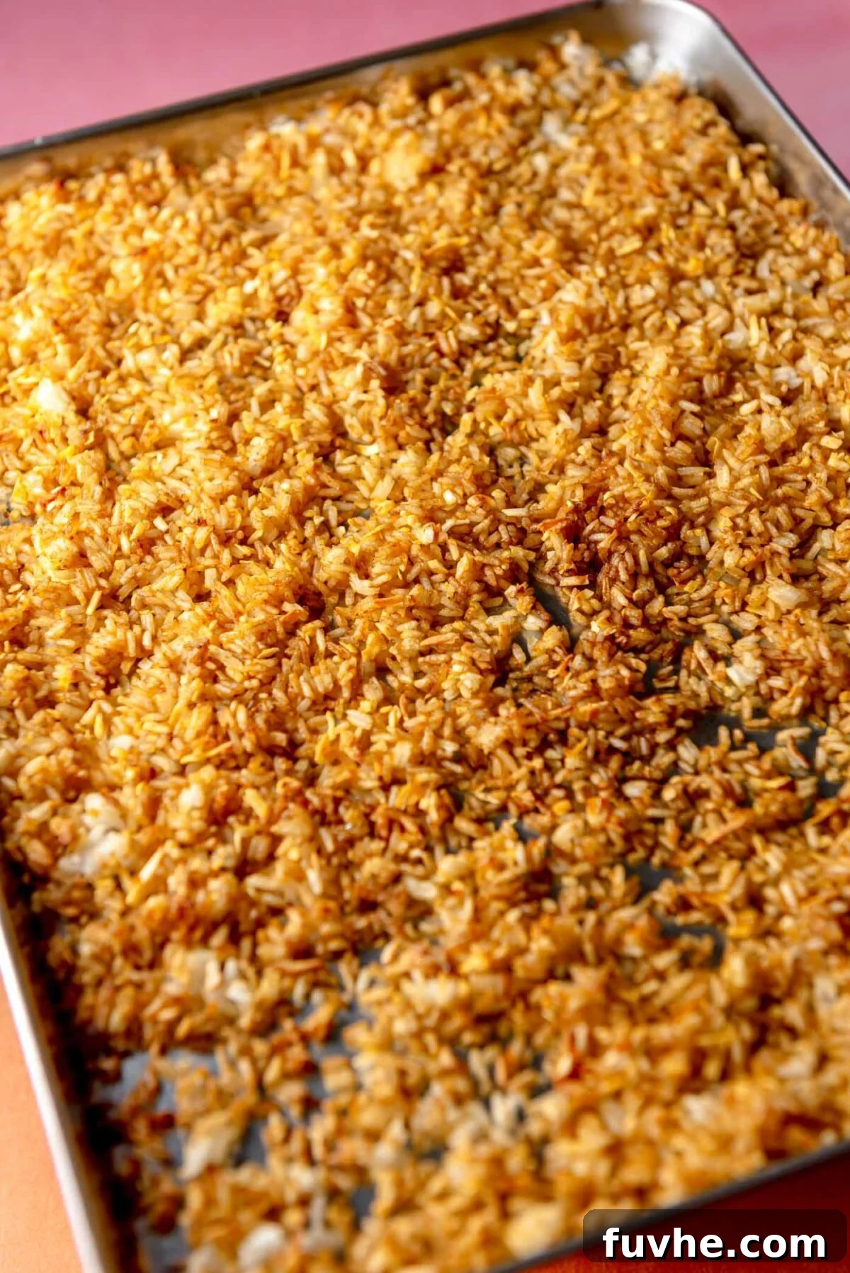 The seasoned rice and coconut mixture evenly spread out on a parchment-lined baking sheet, ready for baking to achieve a crispy texture.