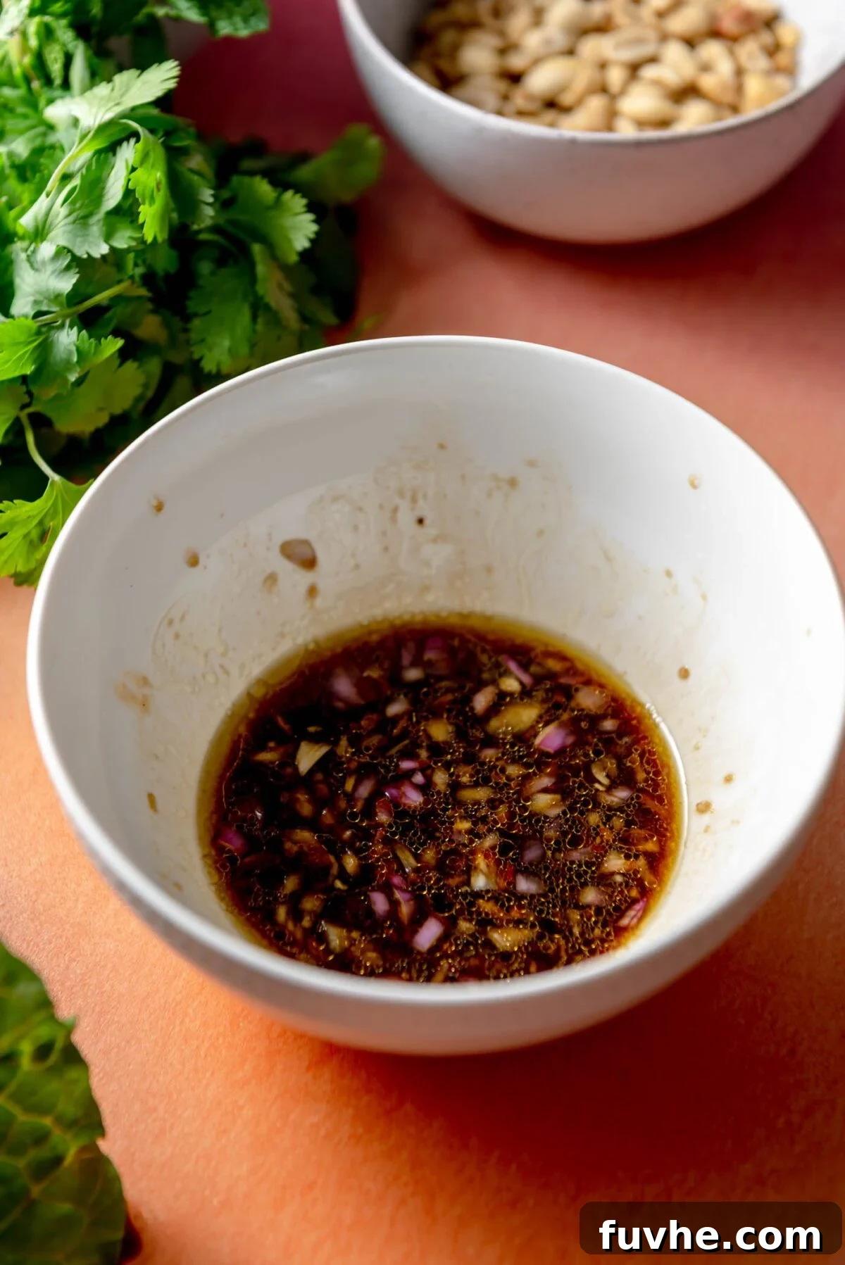 A small dish containing a vibrant salad dressing, whisked together, with visible minced shallot and garlic, ready to be poured over the salad.