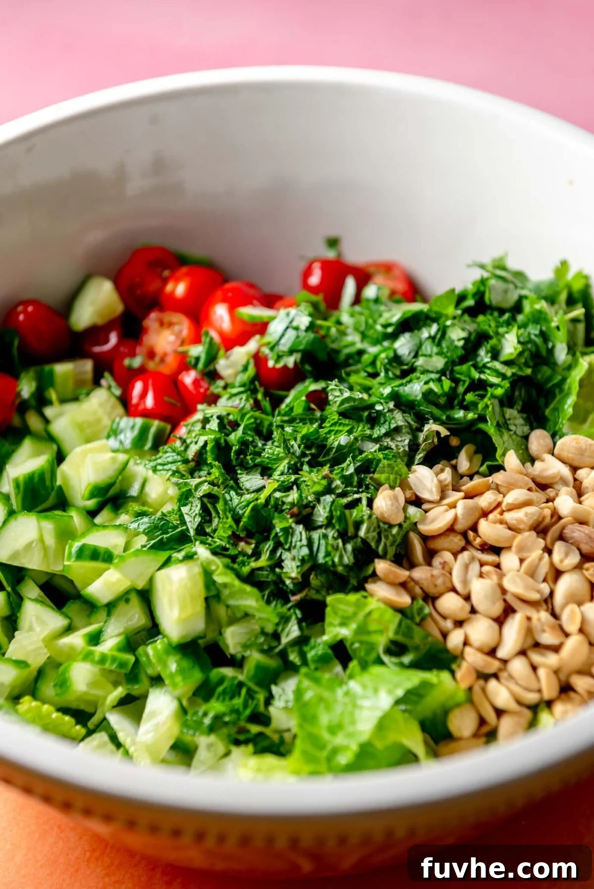 A large bowl filled with crisp lettuce, fresh cucumber, halved cherry tomatoes, finely chopped herbs, and toasted peanuts, forming the base of the crispy rice salad.