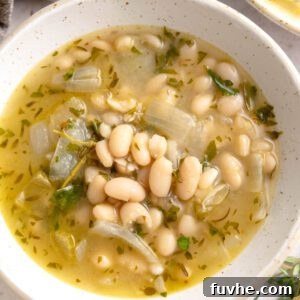 A comforting bowl of brothy white beans, elegantly garnished with fresh chopped herbs and a hint of olive oil, ready to be enjoyed.