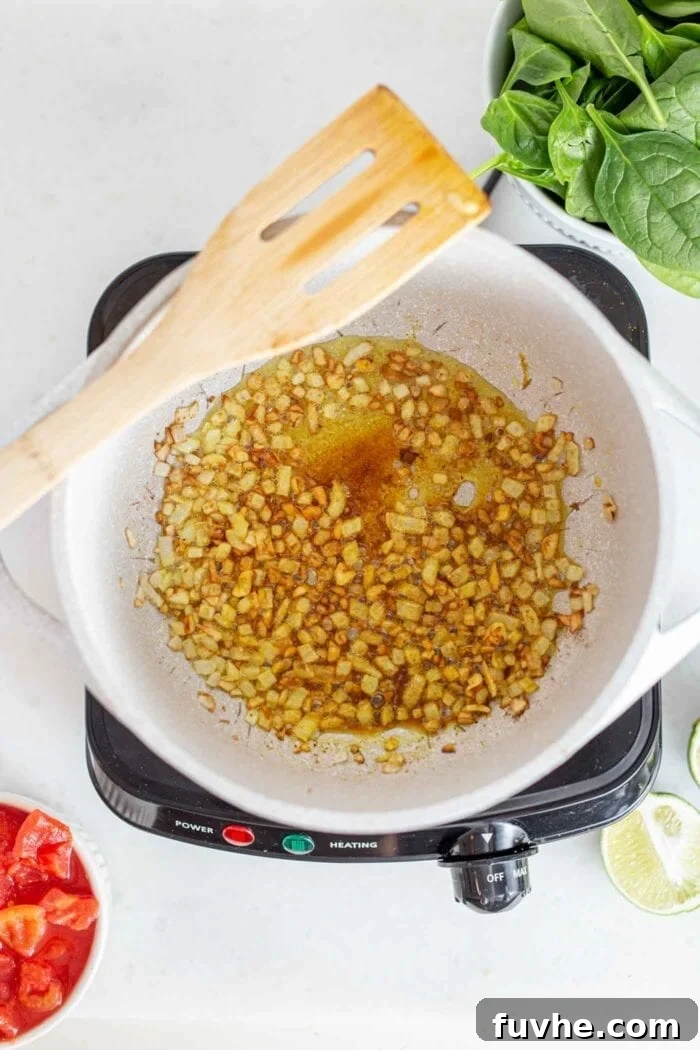 Spices, onions, garlic and ginger cooking in a pot with a wooden spoon.