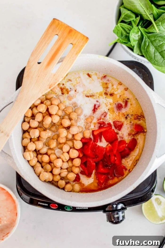 Diced tomato, rice, coconut milk and chickpeas cooking in a pot with a wooden spoon.