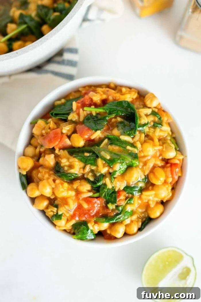 A bowl of chickpea stew with rice, spinach and tomato.