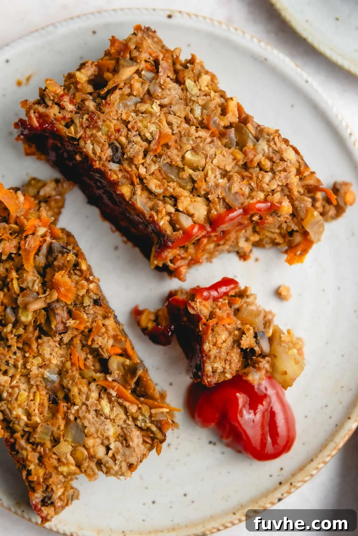 Two generous slices of a perfectly baked lentil loaf, topped with a dollop of vibrant red ketchup, presented on a white plate ready to be enjoyed.