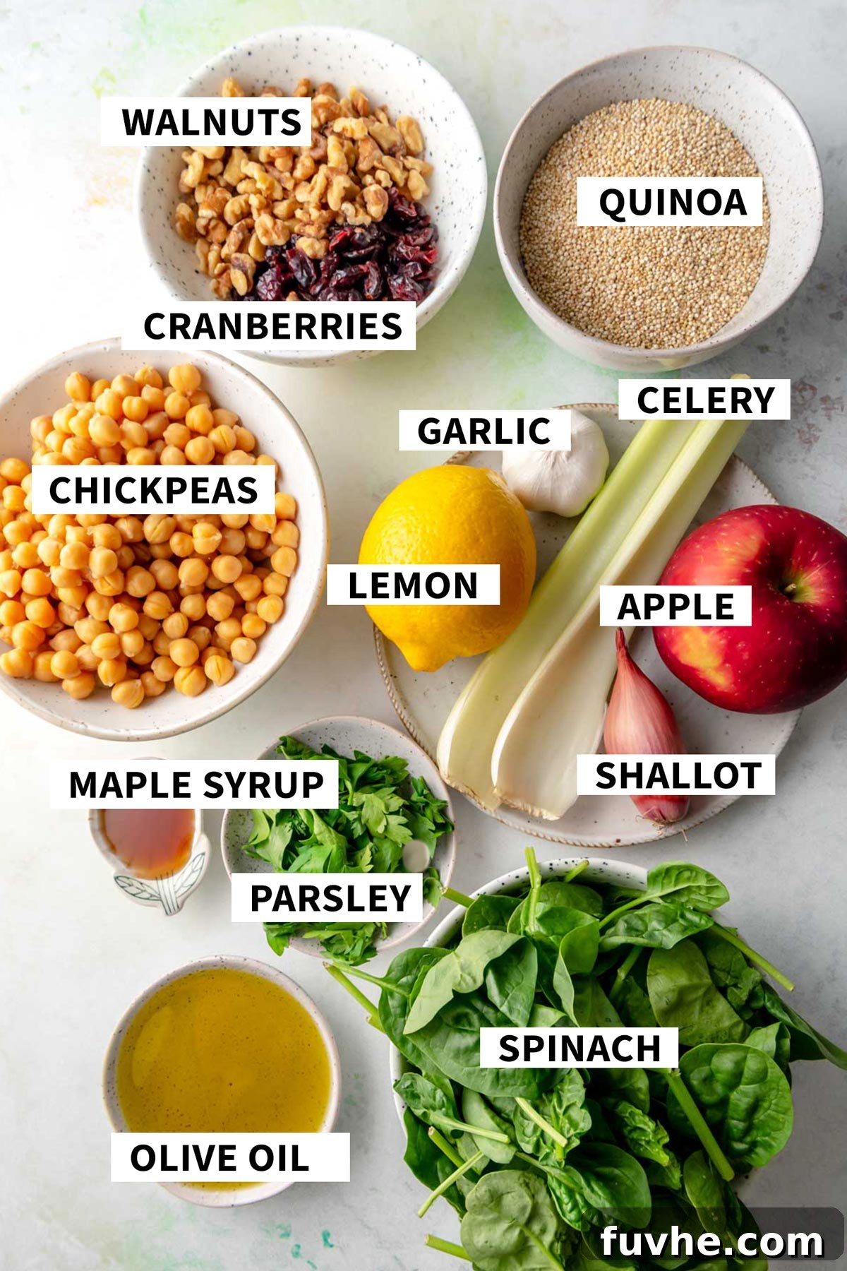 Crisp Apple Quinoa Salad 3 An organized display of fresh ingredients in individual bowls for making Apple Quinoa Salad. Includes quinoa, walnuts, cranberries, chickpeas, lemon, garlic, celery, apple, maple syrup, shallot, parsley, olive oil, and spinach.