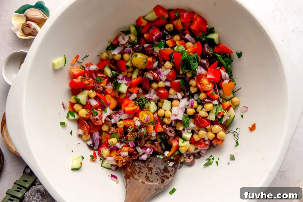 A large mixing bowl brimming with freshly chopped vegetables and herbs: bright red tomatoes, crisp cucumber, finely diced red onion, briny olives, tender chickpeas, and fragrant fresh dill and parsley, awaiting the cooked barley.