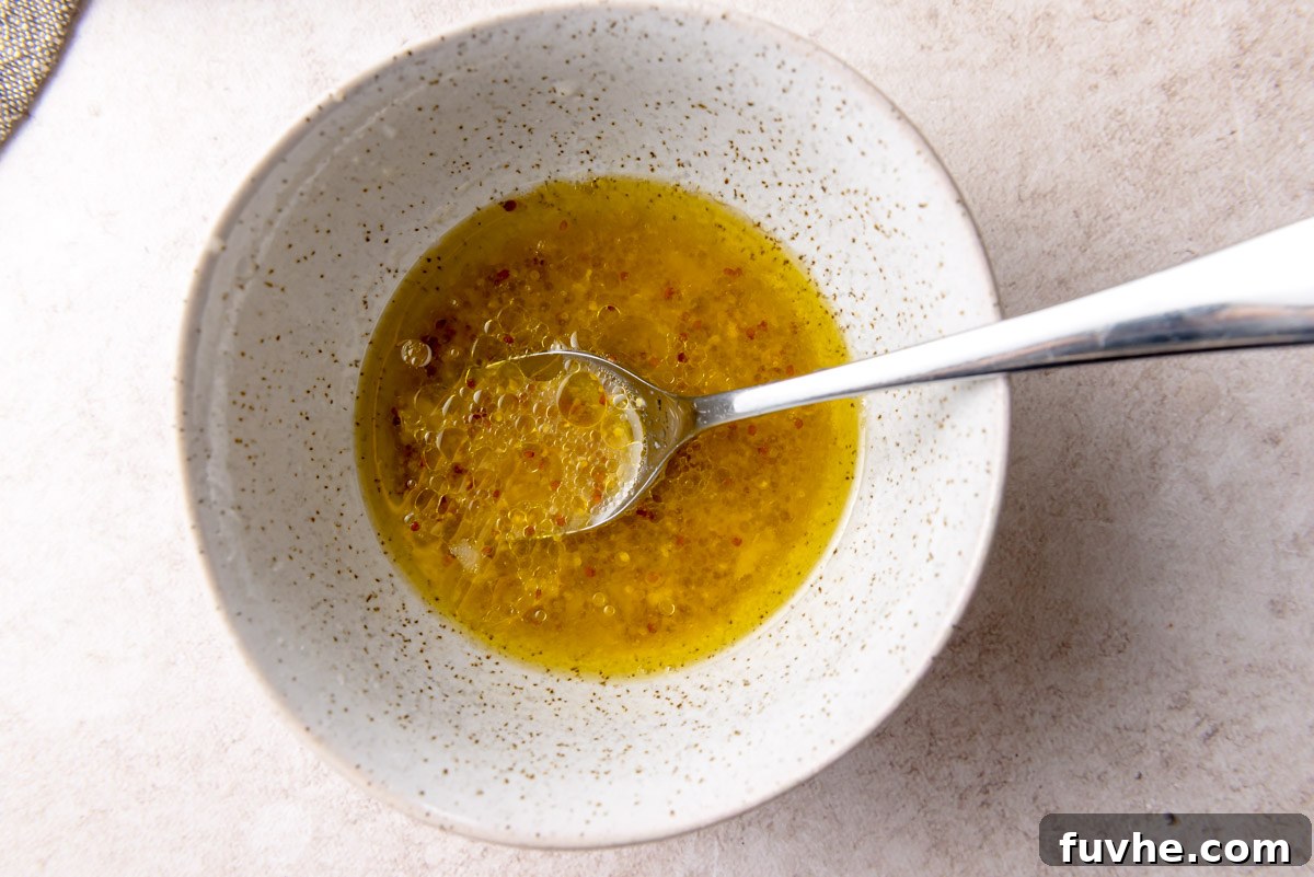 A small, elegant dish containing a vibrant lemon vinaigrette, perfectly emulsified and ready to be drizzled over a fresh salad, with a spoon resting gently inside.