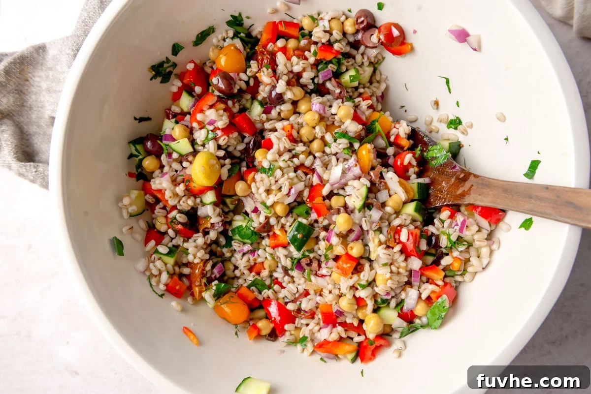 A large, inviting salad bowl showcasing the fully assembled Mediterranean barley salad, a colorful blend of cooked barley, fresh vegetables, chickpeas, olives, and herbs, gently tossed and ready to be served with a wooden spoon.