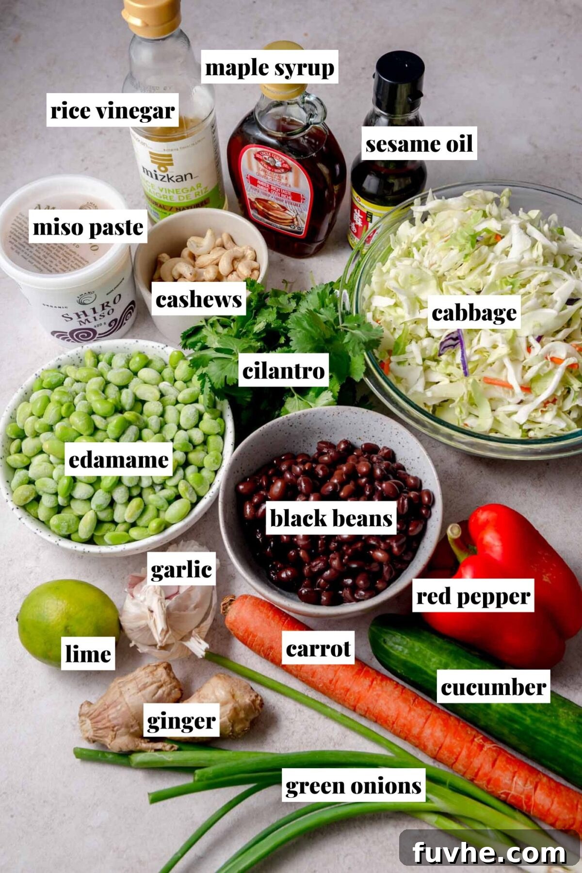 Vibrant Edamame Medley 3 An inviting overhead arrangement of fresh ingredients for the edamame bean salad. Components like shredded cabbage, vibrant red bell pepper, crisp carrot, cool cucumber, aromatic green onions, zesty lime, pungent ginger, fragrant garlic, fresh cilantro, crunchy cashews, bright green edamame, and dark black beans are meticulously laid out. Bottles of rice vinegar, rich sesame oil, and sweet maple syrup are displayed alongside a container of creamy miso paste, each element clearly labeled.