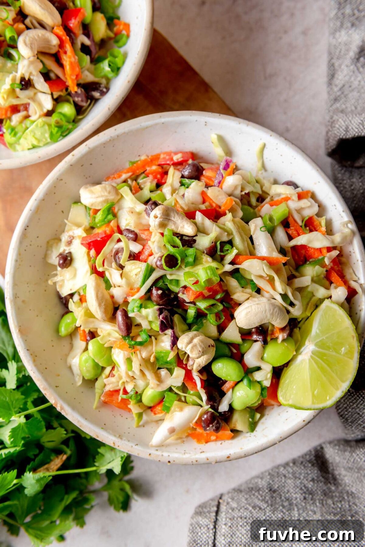 Vibrant Edamame Medley 8 A top-down perspective captures two inviting bowls of the finished edamame bean salad, beautifully garnished with a sprinkle of cashews and chopped green onions, elegantly presented with a fresh lime wedge and sprigs of cilantro on the side.