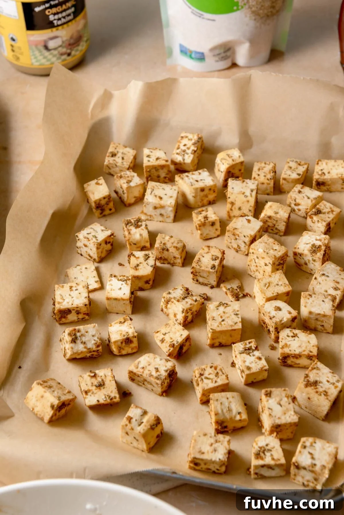 Seasoned tofu cubes, perfectly arranged in a single, even layer on a parchment-lined baking sheet, spaced out for optimal crisping during roasting.