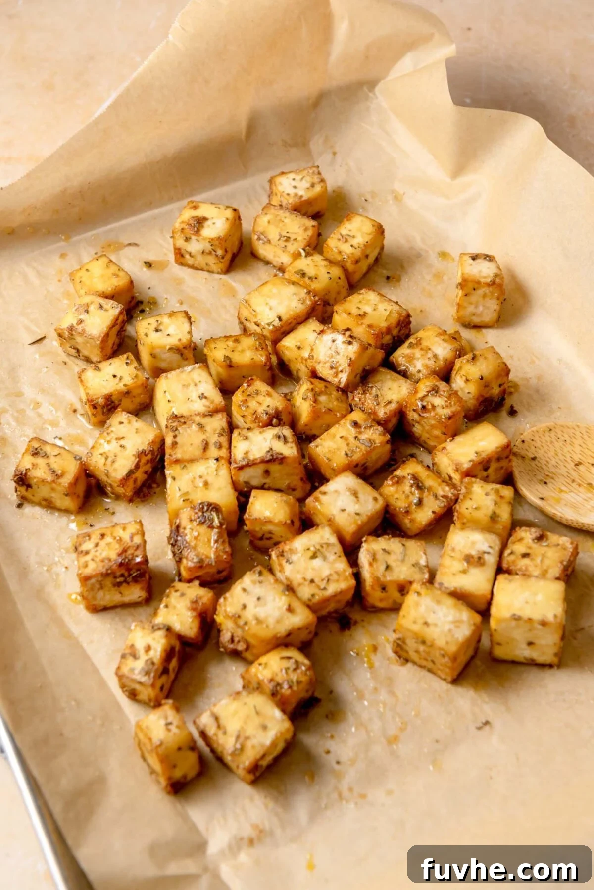 Crispy golden baked tofu cubes, freshly drizzled with a zesty lemon-olive oil mixture and sprinkled with fresh herbs, cooling on a parchment-lined baking pan.