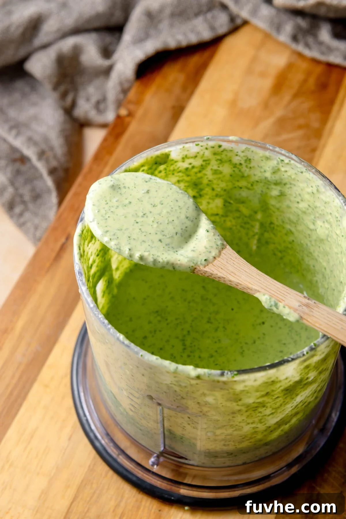 A small blender jar containing the creamy, vibrant green herb tahini sauce, blended with fresh parsley, cilantro, lemon juice, and tahini, showcasing its smooth and inviting texture.