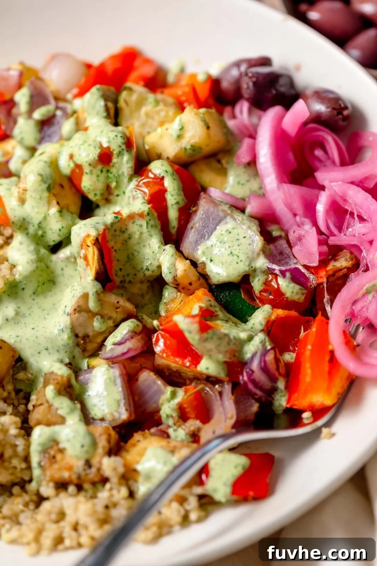 Close-up view of a Mediterranean Roasted Veggie Bowl, beautifully plated with caramelized roasted vegetables, zesty lemon-herb tofu, a generous drizzle of creamy tahini sauce, and garnished with tangy pickled onions and savory olives.