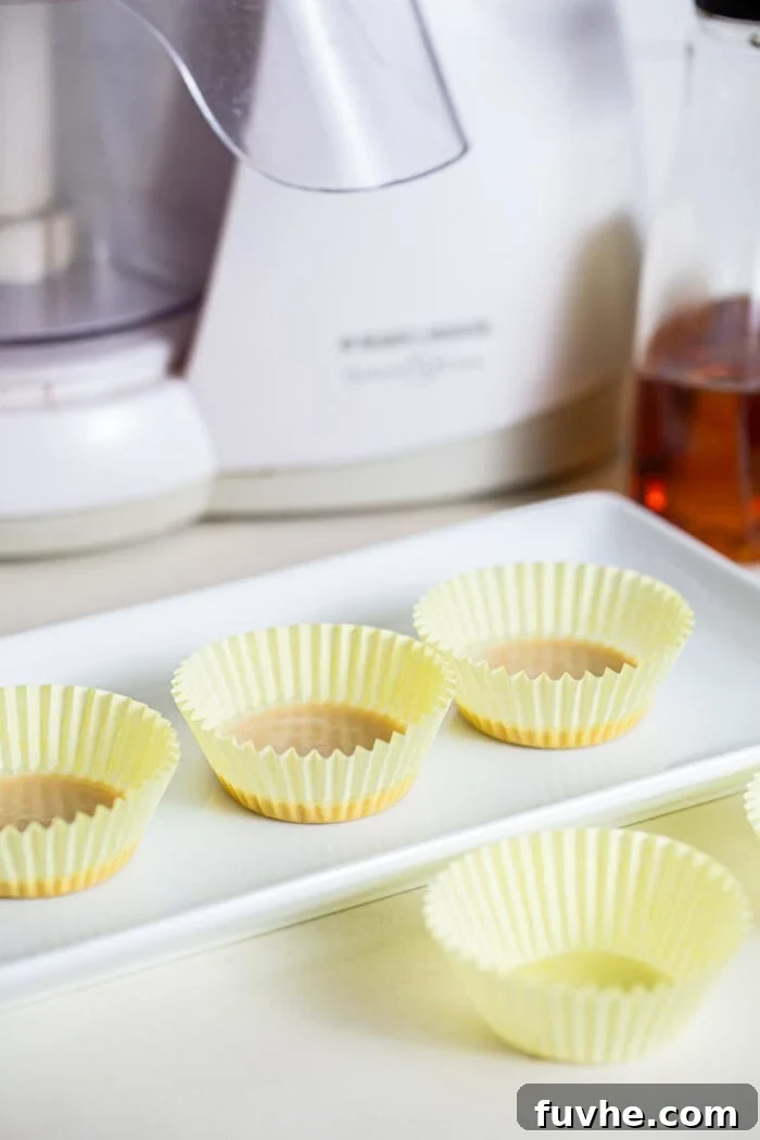 Salted Caramel Tahini Delights 3 Melted coconut oil and tahini mixture evenly distributed into 3 muffin liners, resting on a white plate, ready for freezing.