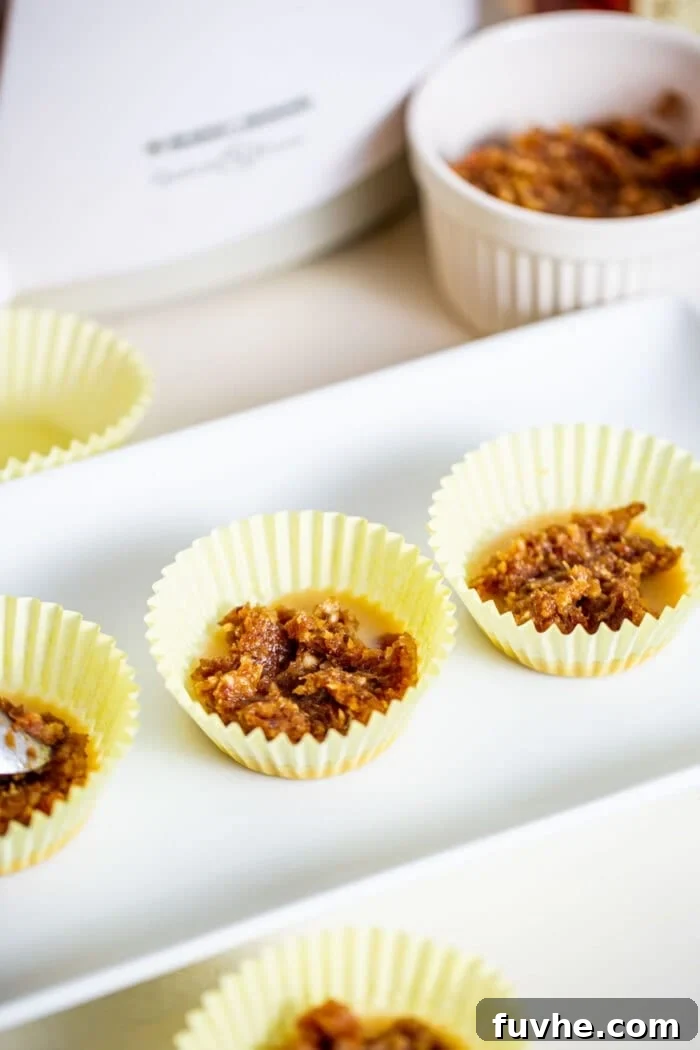 Salted Caramel Tahini Delights 4 A thick, smooth date paste, resembling caramel, portioned into 3 muffin liners on a small white plate, ready to be topped.