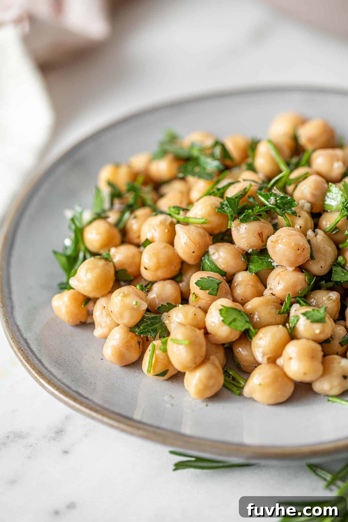 Bright Lemon Garbanzo Salad 2 A beautifully arranged simple lemon chickpea salad on a small white plate, garnished with fresh herbs and a hint of garlic.