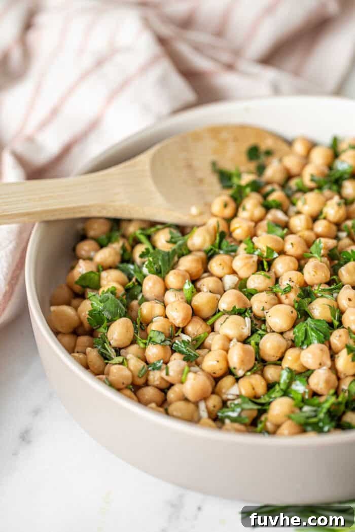 Bright Lemon Garbanzo Salad 4 A serving spoon resting in a bowl of freshly prepared lemon chickpea salad, highlighting its texture and fresh ingredients.