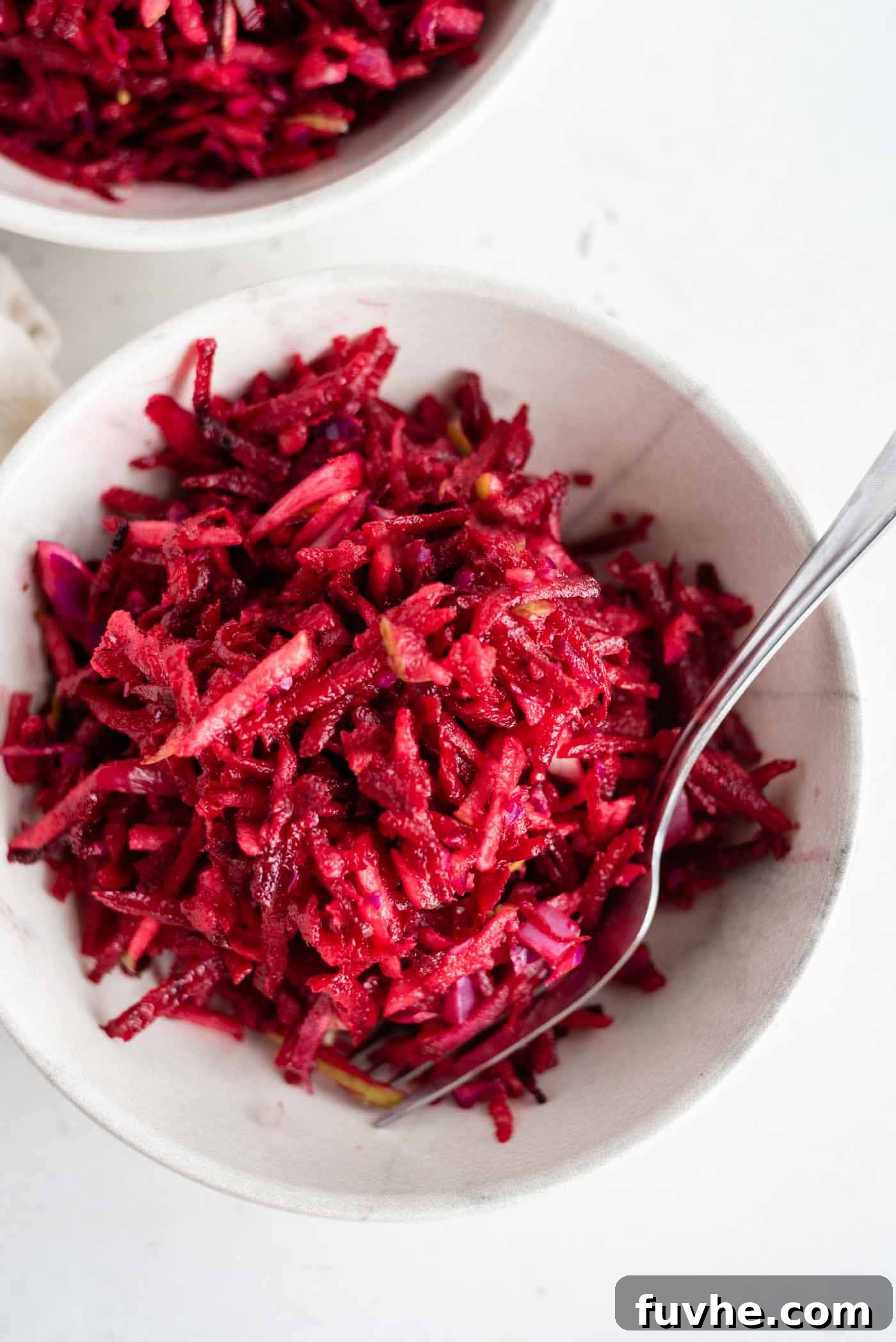 Overhead shot of a beet, apple and cabbage slaw in a bowl with a fork, ready to be served.