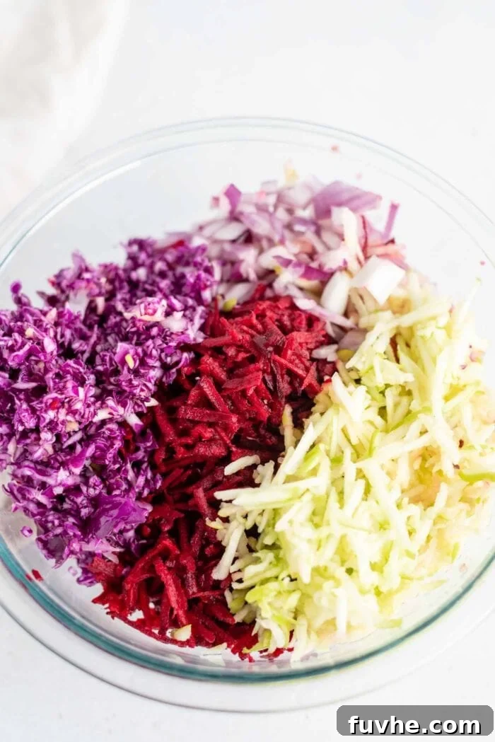 Shredded cabbage, beet, apple and red onion in a large mixing bowl, ready for dressing.