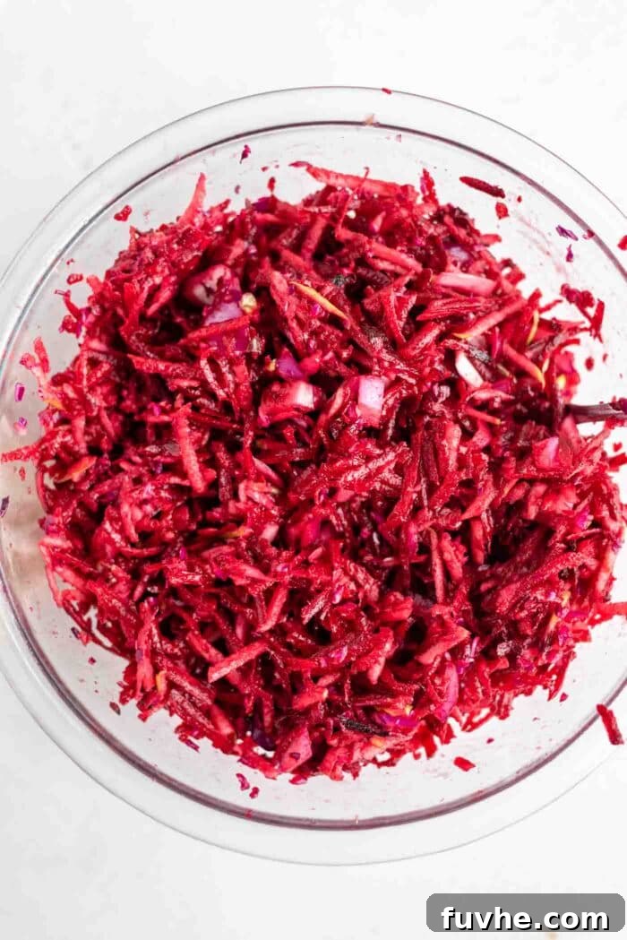 A raw beet, cabbage, and apple salad in a bowl, after being mixed with dressing.