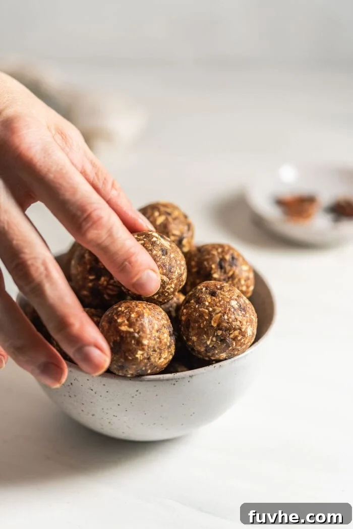 No-Bake Banana Bread Truffles 7 A hand reaching into a bowl filled with beautifully crafted energy balls, poised to pick one up.