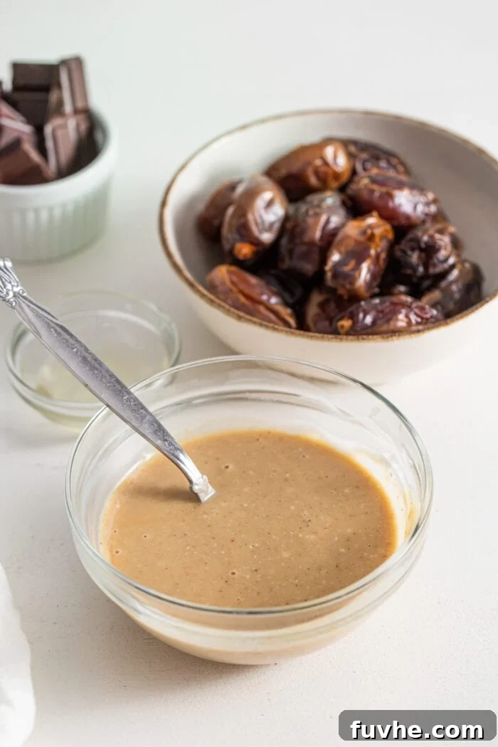 Decadent Chocolate Peanut Butter Dates 5 A small glass bowl brimming with light brown, creamy peanut butter mousse, with a spoon resting in it, ready for filling the dates.