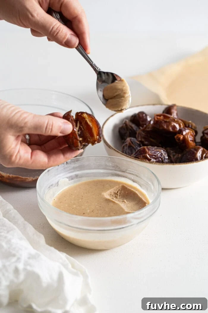 Decadent Chocolate Peanut Butter Dates 6 Hands carefully stuffing a soft Medjool date with creamy peanut butter mousse using a small spoon, with more dates awaiting their turn.